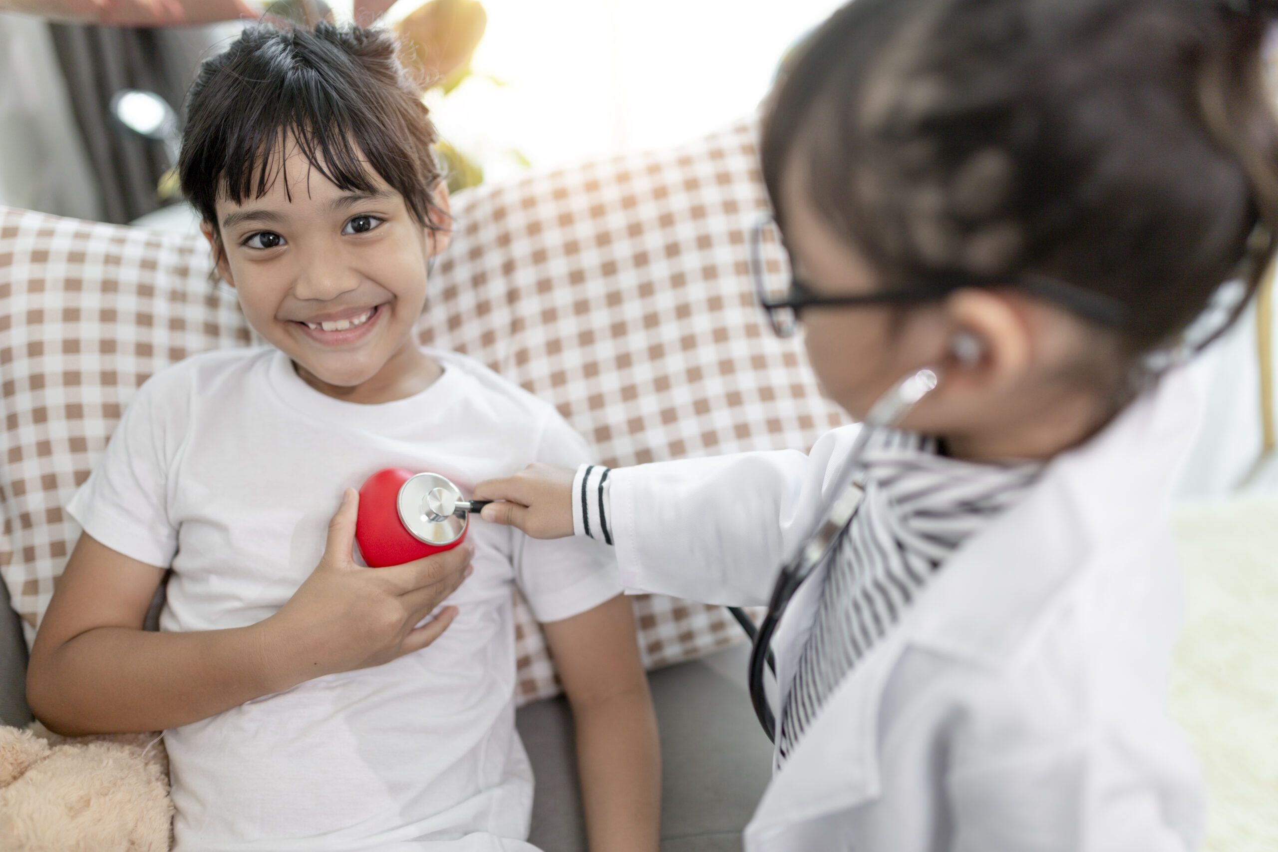 Two cute children play doctor and hospital using stethoscope. Friends girls having fun at home or preschool.